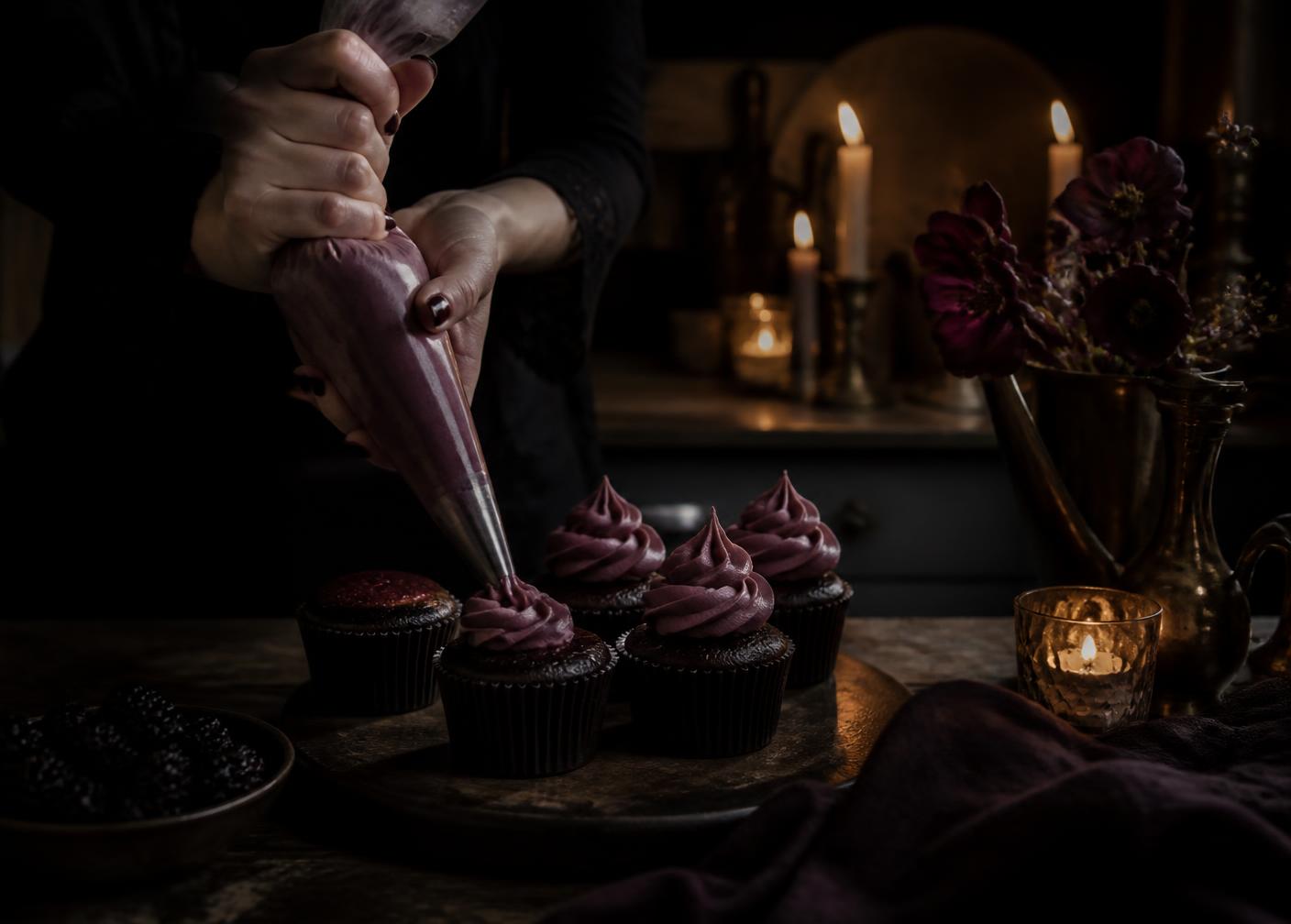 Piping dark buttercream onto cupcakes in a candlelit kitchen at night